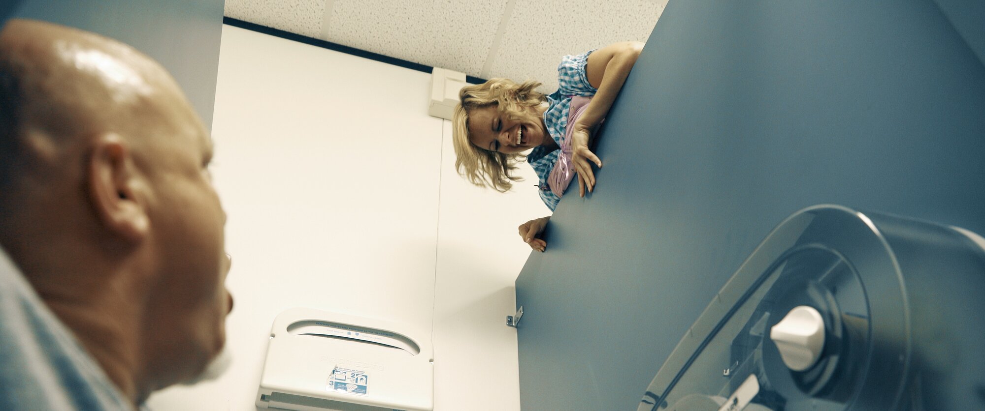 Maria peeks over a bathroom stall