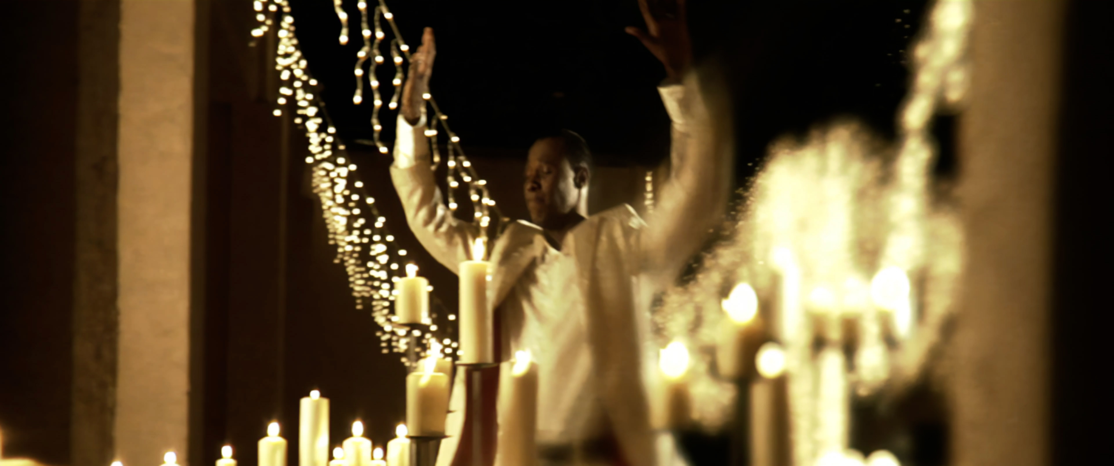 Micah Stampley with candles and string lights, arms raised &mdash; I Believe